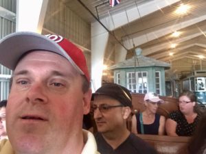 Inside museum on trolley car ride, Mark taking a selfie and Roland is sitting behind him