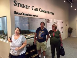 Street Car Communities sign overhead with a trolley car display in a glass box, standing in front from left to right is Roz, Rick and Jane