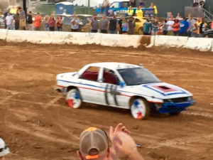 White car with thin blue and red lines on the side, squared bolder blue, and red on the front, tires have the color blue and red in a triangle pointing towards the center 