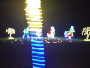 On the left is whit tree, in the center are four skaters, on the left is a skater in green and blue light and white light for skates. Second one can't been seen due to a white and blue strip of lights kind of like beaded down the picture. The third is in red, and white light, and the foruth are two skaters together, one is green and other in red. On the right is another yellow light tree