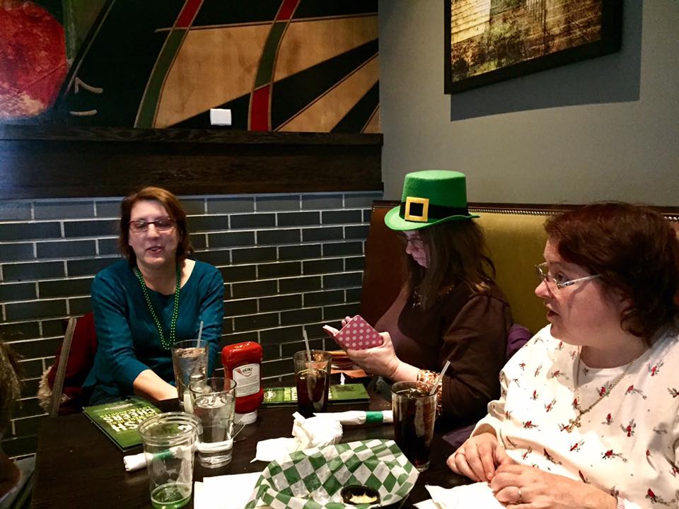 Picture of Jane, on left almost cneter, Carla looking at her phone on right wearing green Irish hat and Angie front right